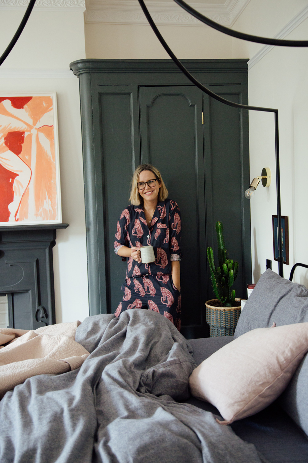 Alexandra Stedman wearing Desmond & Dempsey pyjamas in her bedroom whilst drinking a coffee.